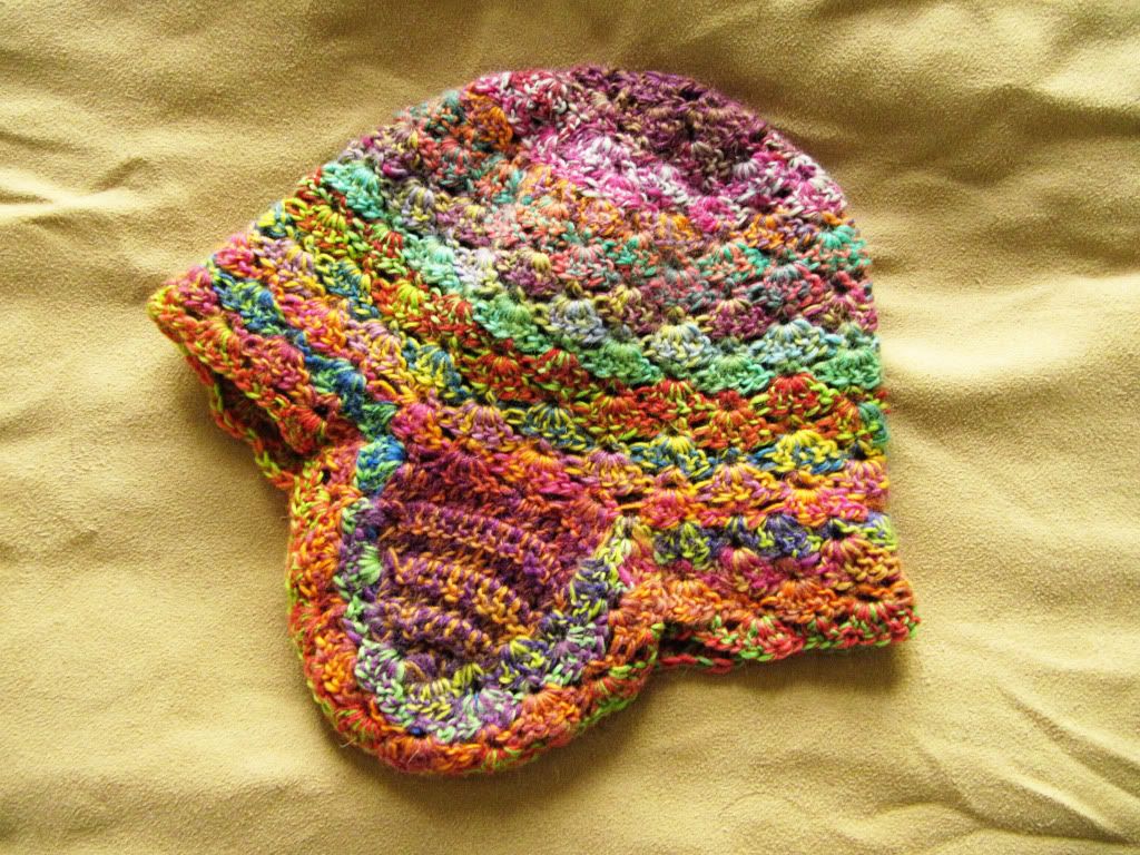 Multi-colored lacy earflap hat laying on a tan surface.